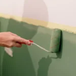 Person applying green paint roller to wall during home decorating