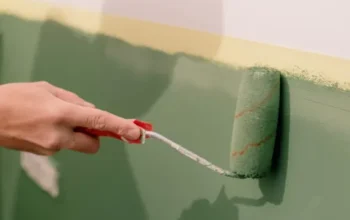 Person applying green paint roller to wall during home decorating