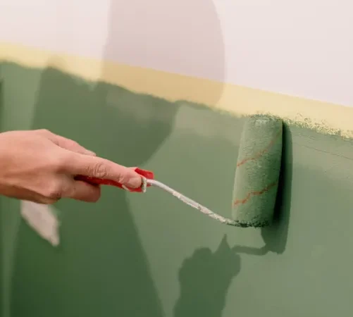 Person applying green paint roller to wall during home decorating